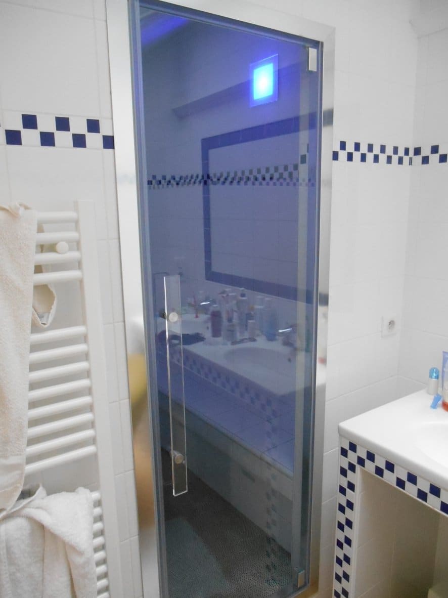 Porte vitrée de hammam ouverte sur la salle de bains avec sèche-serviettes